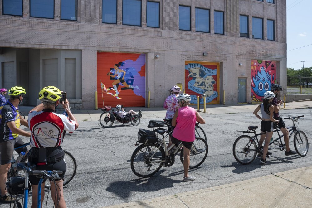 在欧几里得大道4600号，骑自行车的人正在欣赏艺术家Julia Kuo、April Bleakney和Jordan Wong &Chad Fedorovich创作的壁画(从左至右)。