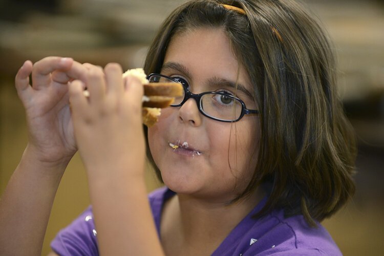 在雷克伍德社区服务中心为幼儿园到五年级学生发起的夏季午餐和丰富项目中，一个孩子正在享受她的三明治。